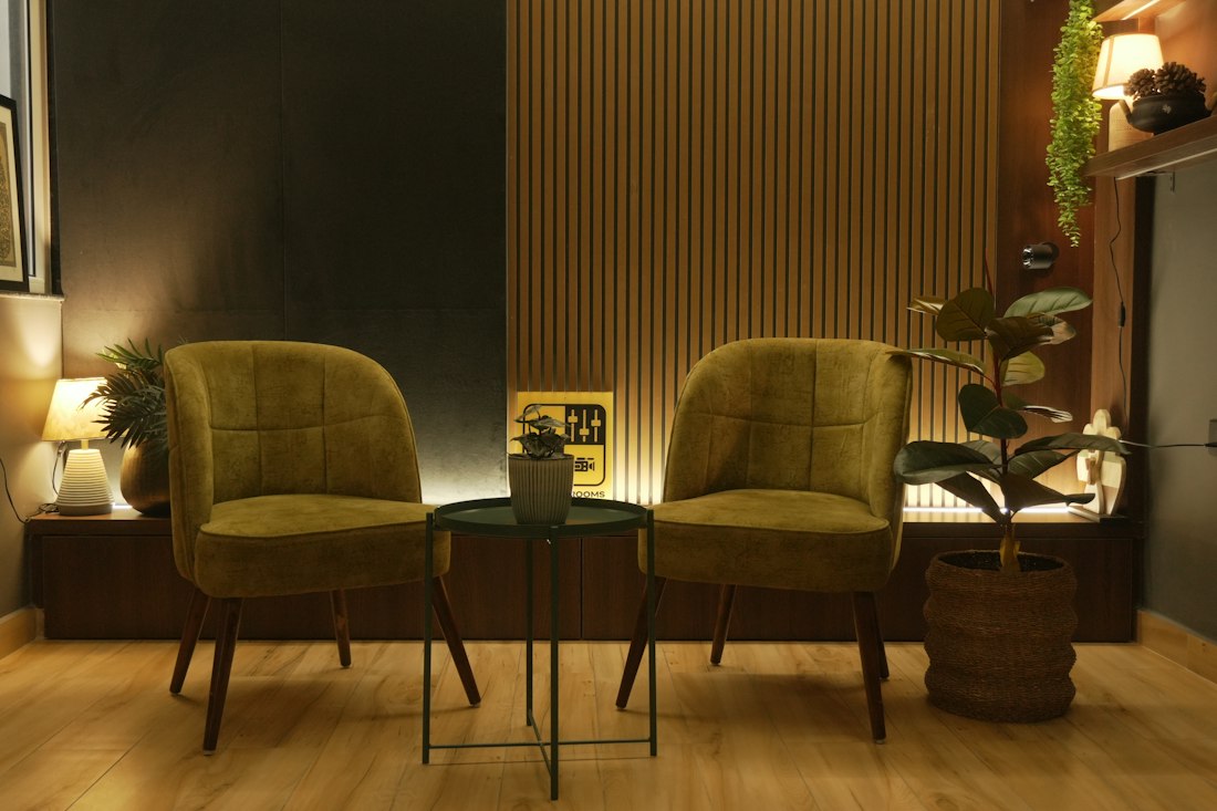 Cantinho de espera com poltronas estofadas, mesa lateral, plantas e luz acolhedora
